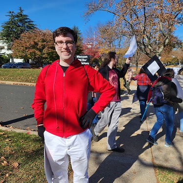 Person in a red coat and white pants at a picket line, smiling at camera.